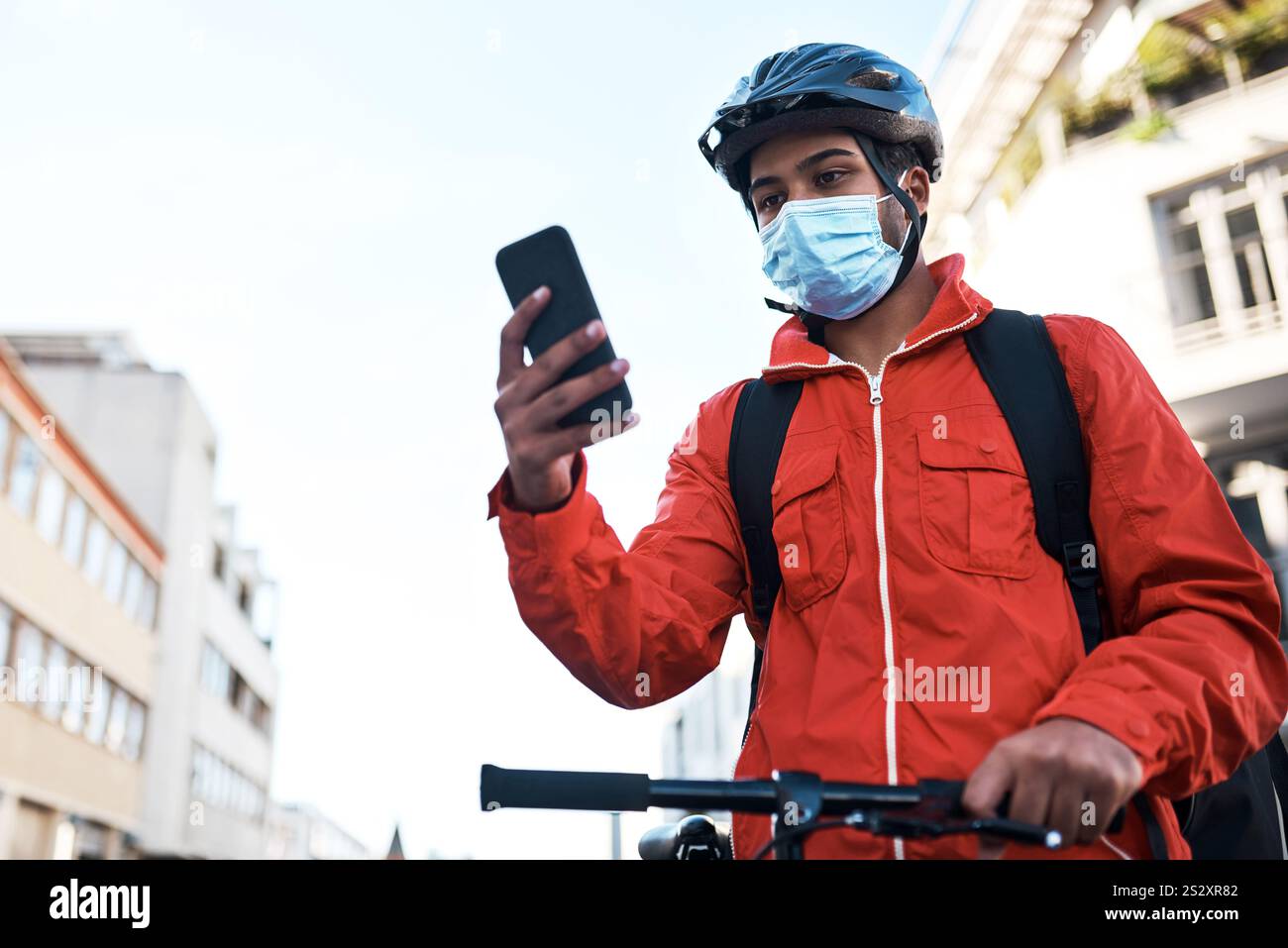 Telefon, Fahrrad und Lieferer mit Maske in der Stadt für E-Commerce, Kurier oder Transportservice. Technologie, Fahrrad und männlicher Frachtarbeiter mit Handy Stockfoto