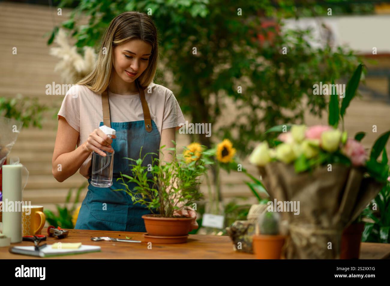 Floristin, die in einem Blumenladen arbeitet und sich um eine Pflanze kümmert, während sie neben dem Theken steht, umgeben von Blumen und Pflanzen in einem Blumenladen Stockfoto