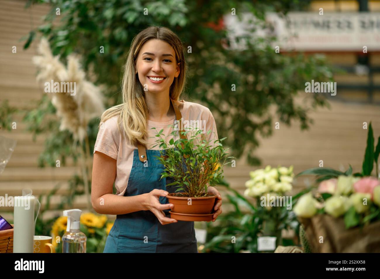 Floristin, die in einem Blumenladen arbeitet und sich um eine Pflanze kümmert, während sie neben dem Theken steht, umgeben von Blumen und Pflanzen in einem Blumenladen Stockfoto