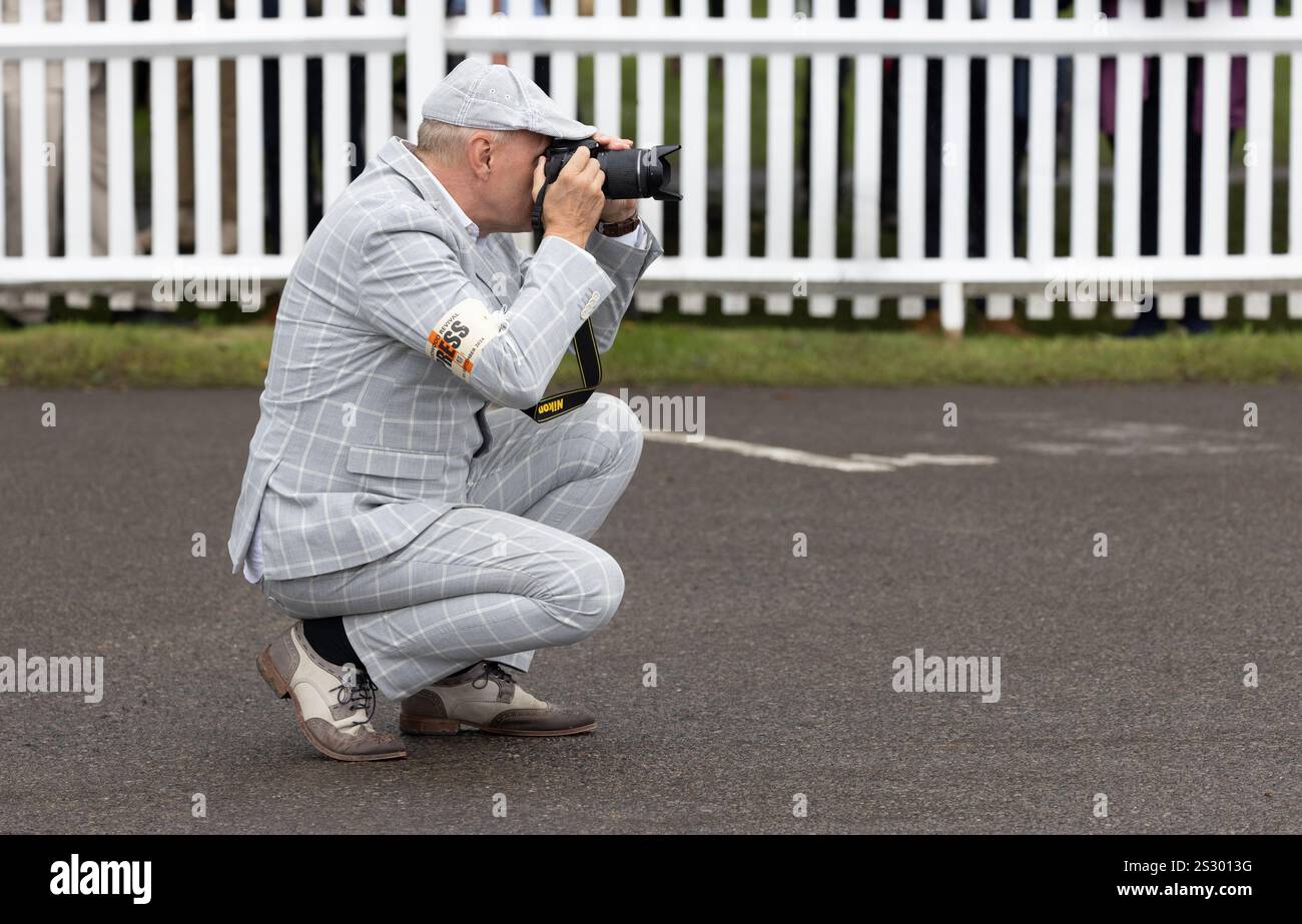 Gut gekleideter Gentleman mit grauem Karomuster und passender Mütze mit zweifarbigen Schuhen. Mit einem PRESSEETIKETT um den Arm und Fotos machen. Goodwood Stockfoto
