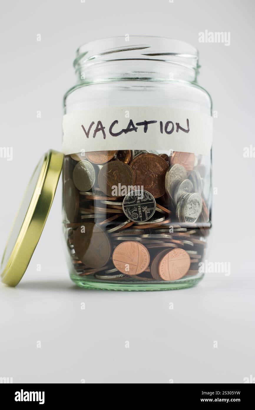 Ein Glasgefäß mit Münzen mit einem handgeschriebenen Etikett, das das Geld anzeigt, das für einen Urlaub reserviert wurde Stockfoto