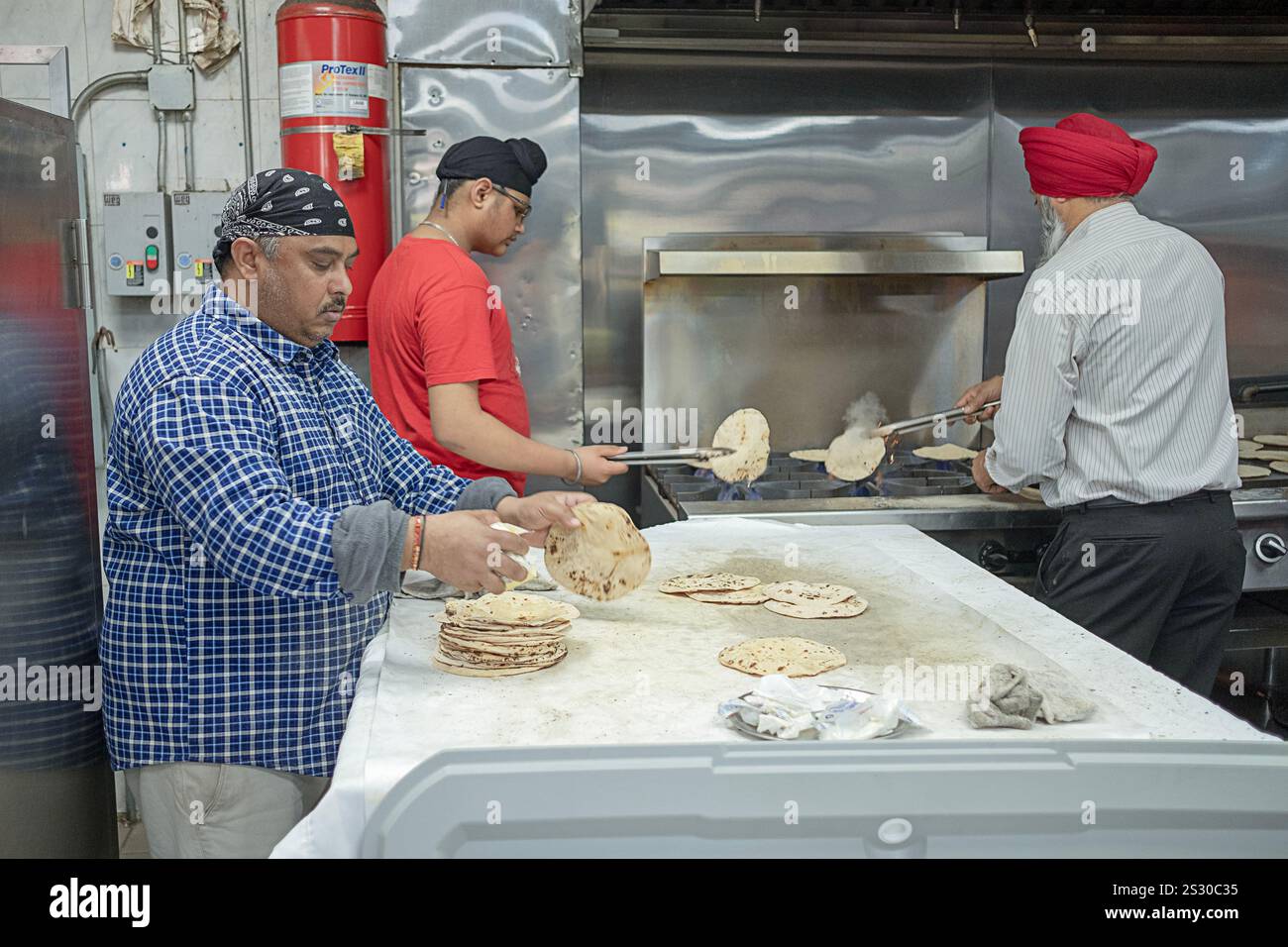 Gläubige Sikh-Männer veredelten neu zubereitetes Roti-Brot unter dem Tempellangar in South Richmond Hill Queens, New York. Stockfoto