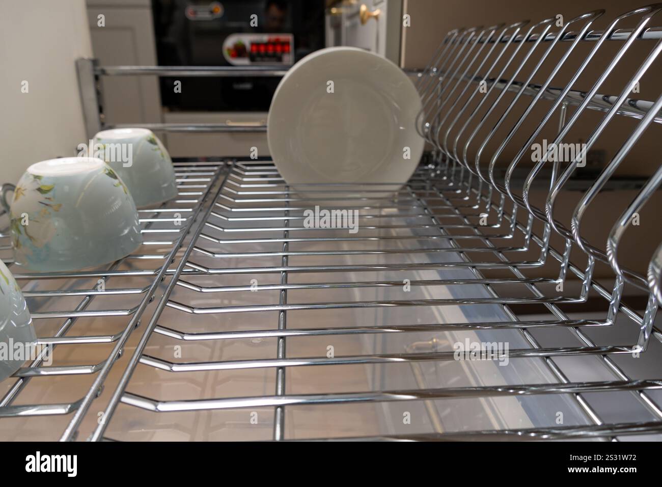 Eine saubere und organisierte Kücheneinrichtung mit einem Chrom-Geschirrständer mit Tellern und Tassen. Perfekt, um moderne Küchenästhetik und Funktionalität zu präsentieren Stockfoto