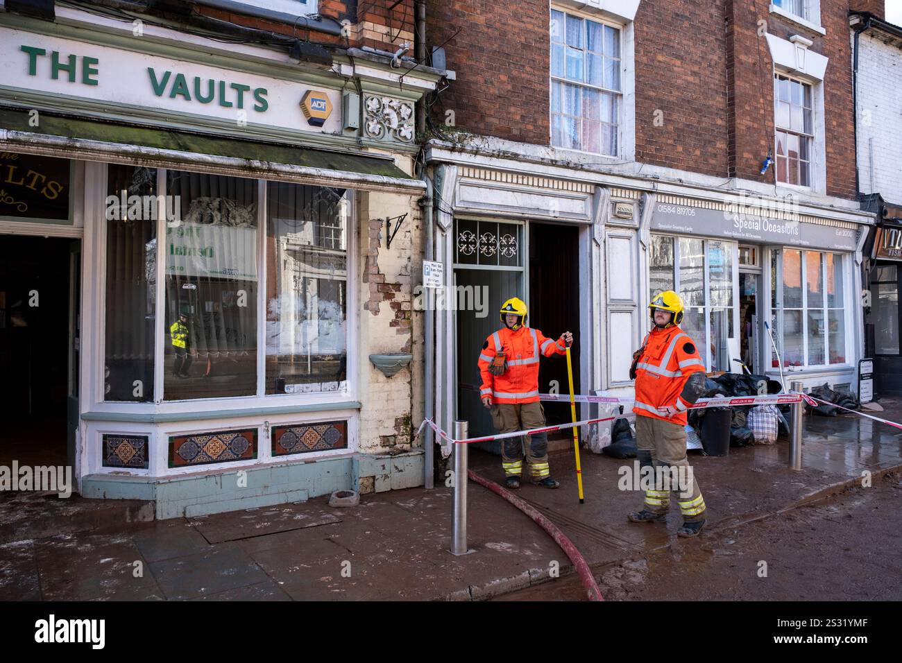 Die Rettungsdienste sind dabei, Wasser aus dem Untergeschoss des Vaults Pubs und einem benachbarten Grundstück zu pumpen, während die Menschen in der Stadt Tenbury Wells in Worcestershire nach den Überschwemmungen während des Sturms Bert am 25. November 2024 in Tenbury Wells, Großbritannien, Schlamm und Schlamm säubern. Als starke Regenfälle von Sturm Bert in ganz Großbritannien einschlugen, überflutete Tenbury Wells die Stadt, nachdem der Wasserspiegel am Kyre Brook stieg, was dazu führte, dass eine Mauer an der Market Street einbrach, sodass Hochwasser die Stadt füllen konnte und Grundstücke überschwemmte. Ein weiterer Schaden wurde durch den Überflutungsvorgang eines Traktors verursacht Stockfoto