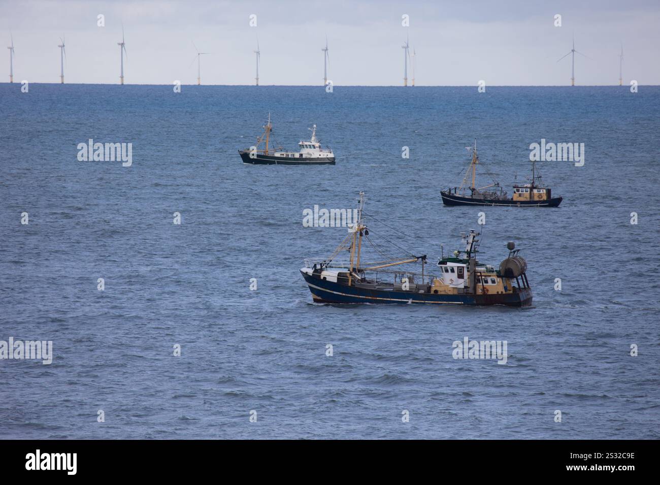 Drei Fischereifahrzeuge vor einem Offshore-Windpark in der Nordsee nahe Egmond aan Zee an einem klaren Tag Stockfoto