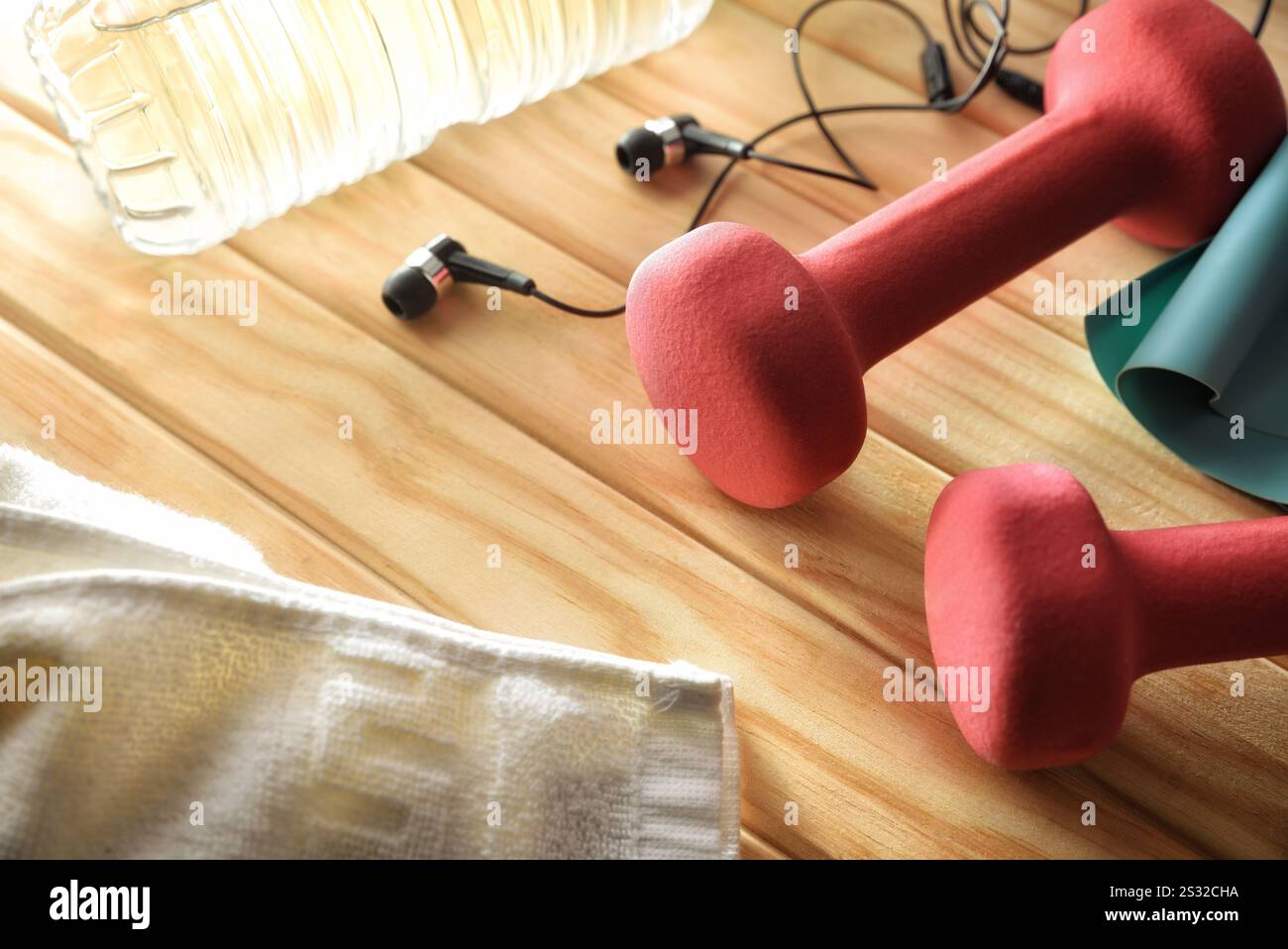Frau Sport Training Routine Konzept und Unterhaltung mit rosa Kurzhanteln auf Holzlatten mit Ohrhörern Wasserflasche und Handtuch. Erhöhte Aussicht. Stockfoto