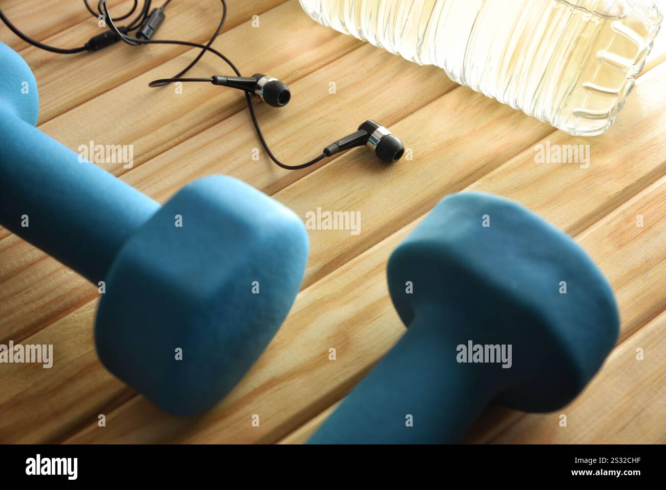 Gesundes und entspannendes Lifestyle-Konzept aus Musik und Sport mit in-Ear-Kopfhörern und blauen Kurzhanteln auf Holzlatten mit einer Flasche Wasser. Erhöhter Durchblick Stockfoto