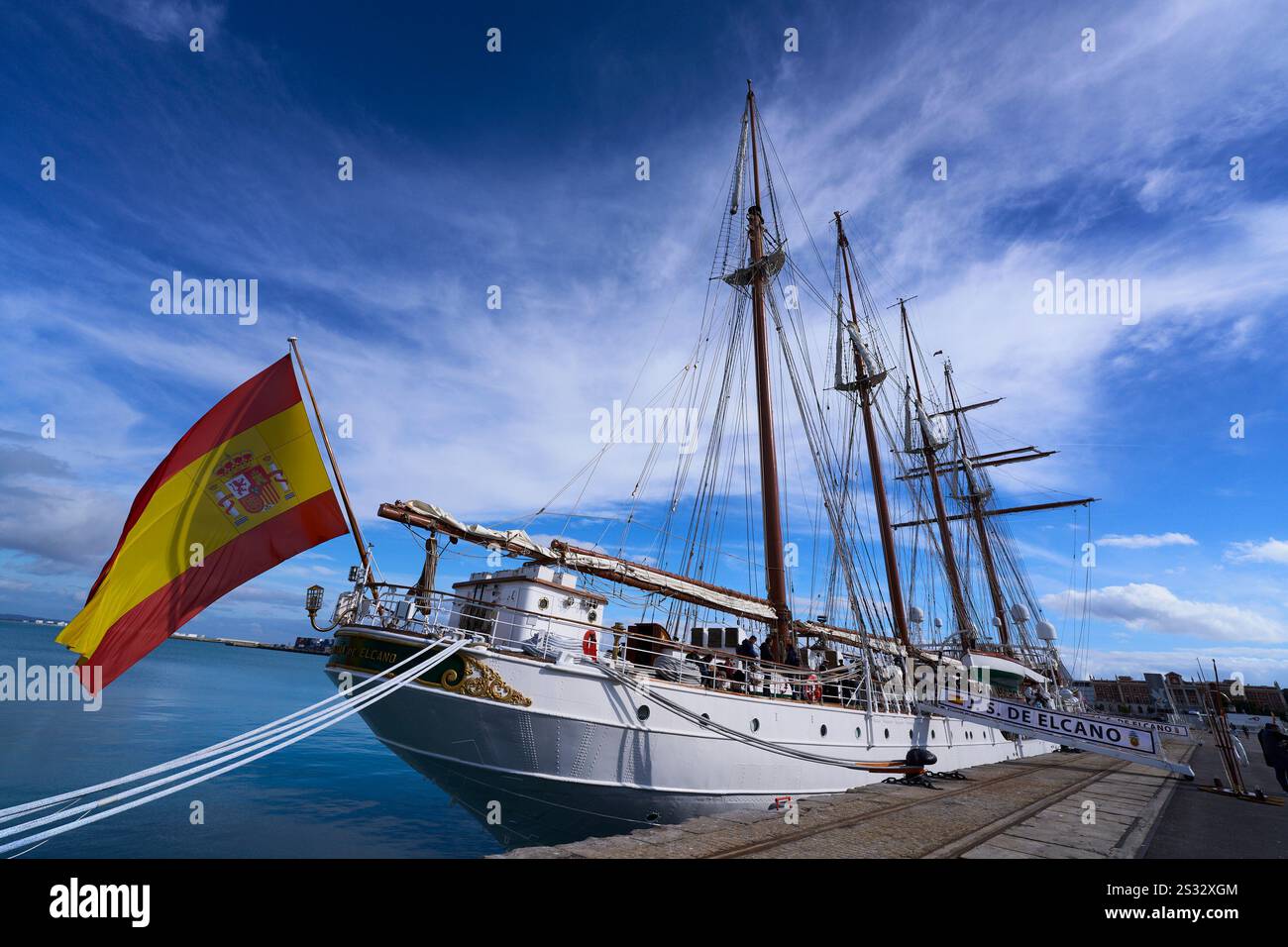 Bilder der Juan Sebastián de Elcano, dem legendären Ausbildungsschiff der spanischen Marine, legten am 8. Januar 2025 im Hafen von Cádiz an. Der majestätische Viermast-Schoner glänzt unter der Wintersonne, mit seinem weißen Rumpf und den polierten Holzdecks, die jahrhundertelange maritime Tradition widerspiegeln. Die Segel sind ordentlich gerollt und zeigen die komplizierte Takelage und die hohen Masten, die die Skyline dominieren. Crew-Mitglieder in formellen Marineuniformen können beobachtet werden, wie sie sich auf Zeremonien vorbereiten und ein Gefühl von Größe und Stolz hinzufügen. Die spanische Flagge des Schiffes flattert in der sanften Brise, während die historische Architektur des Hafens A Stockfoto