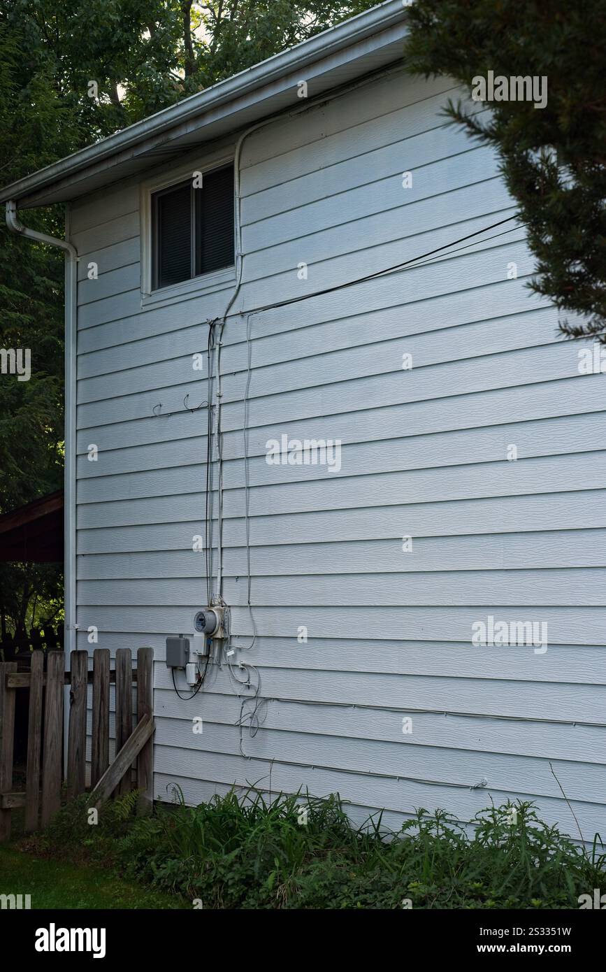 Seitenwand eines zweistöckigen Hauses, verkleidet mit altem Aluminium und schmutzigen Dachrinnen Stockfoto