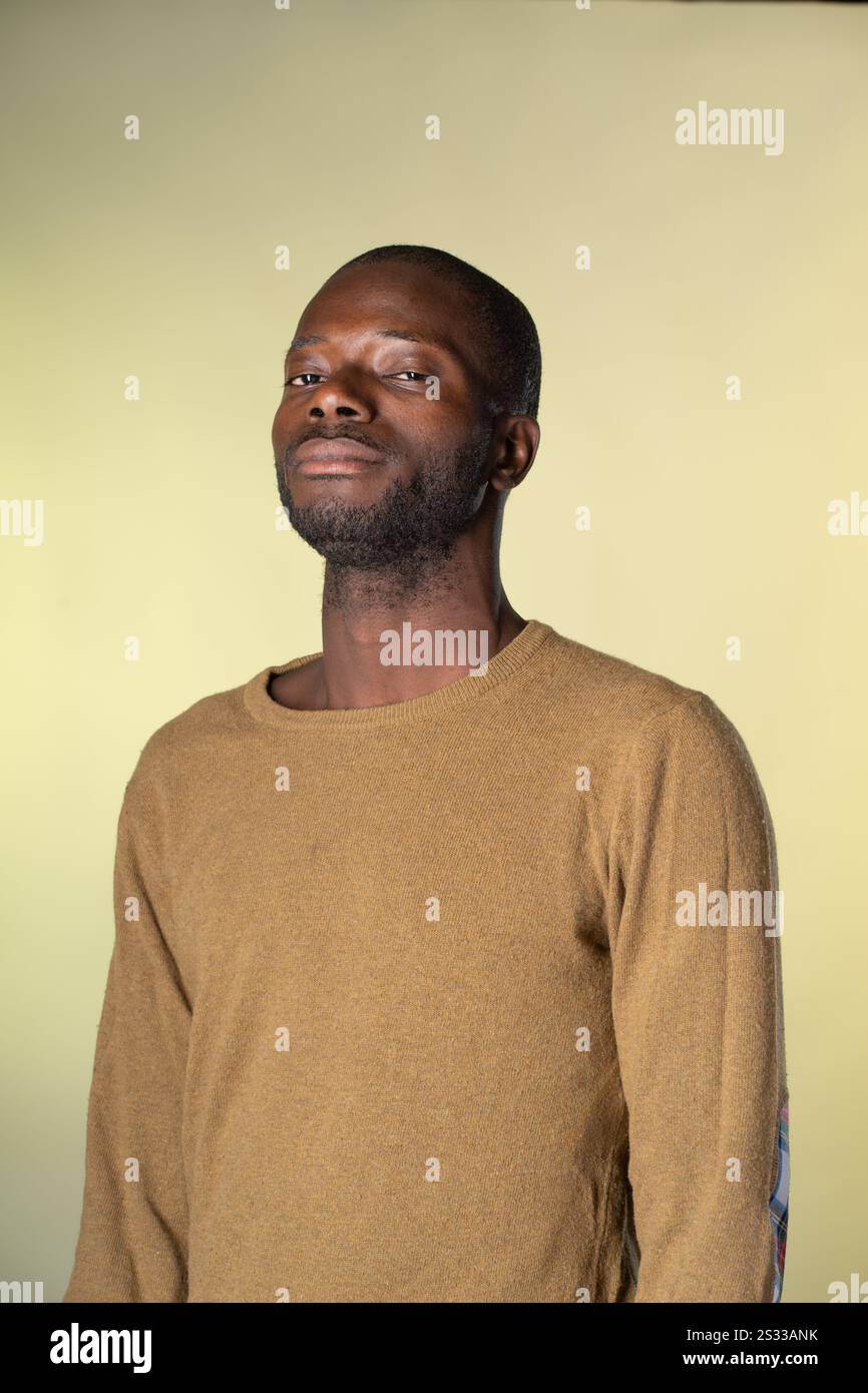 Ein selbstbewusster afrikanischer Mann in einem lässigen Pullover, der vor einem gelben Hintergrund steht und mit einer selbstbewussten und gelassenen Exp in die Kamera blickt Stockfoto