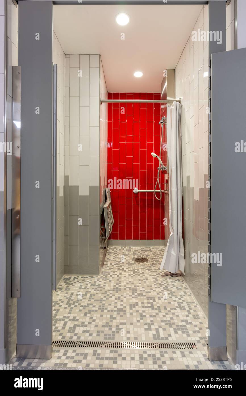 Vertikales Foto einer neuen privaten Dusche im Fitnessraum mit roter gefliester Wand, Bank, gefliestem Boden und weißem Duschvorhang. Stockfoto