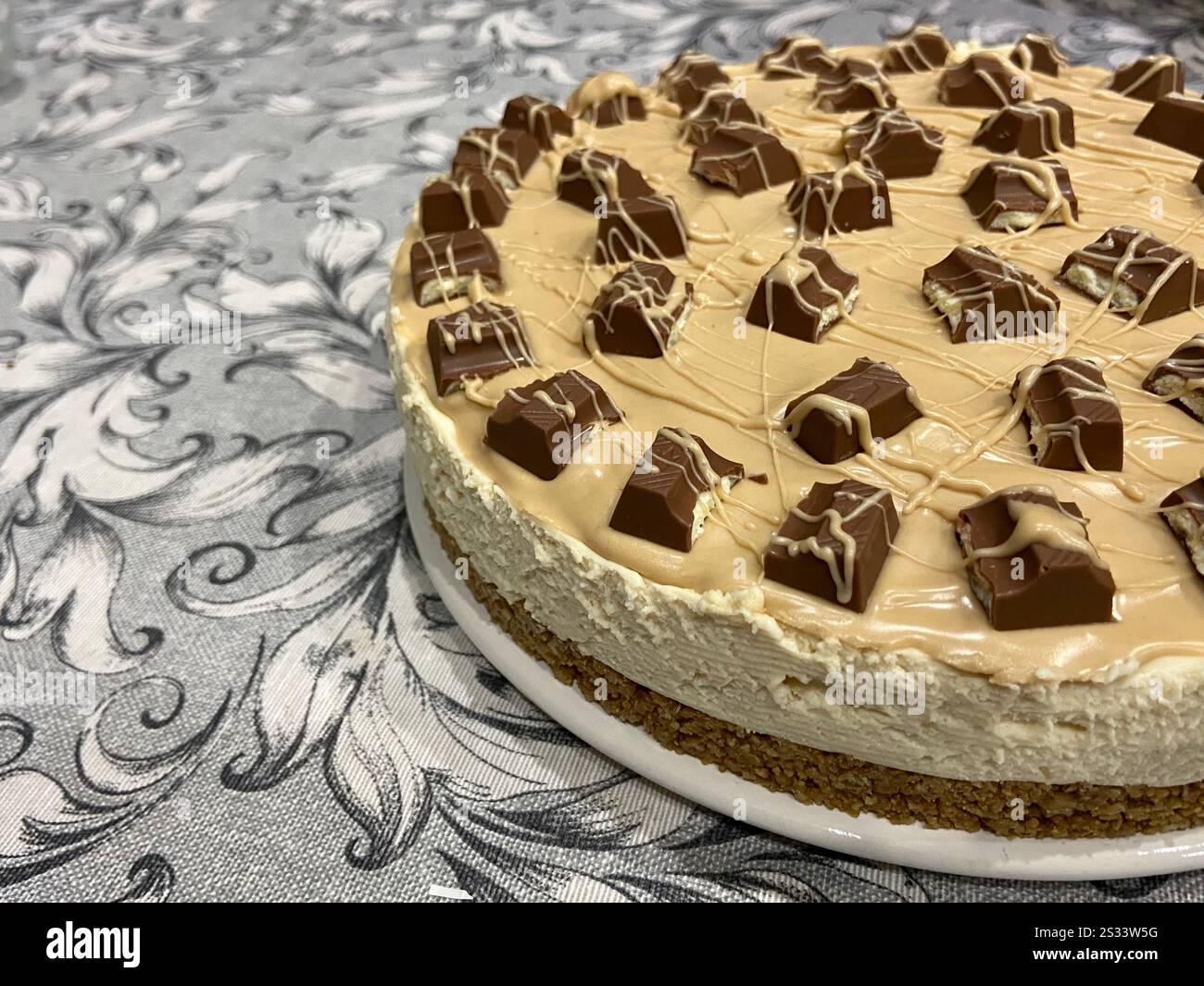 No-Bake Karamell Cheesecake mit Schokoladenbelag auf dekorativer Tischdecke, Nahperspektive Stockfoto