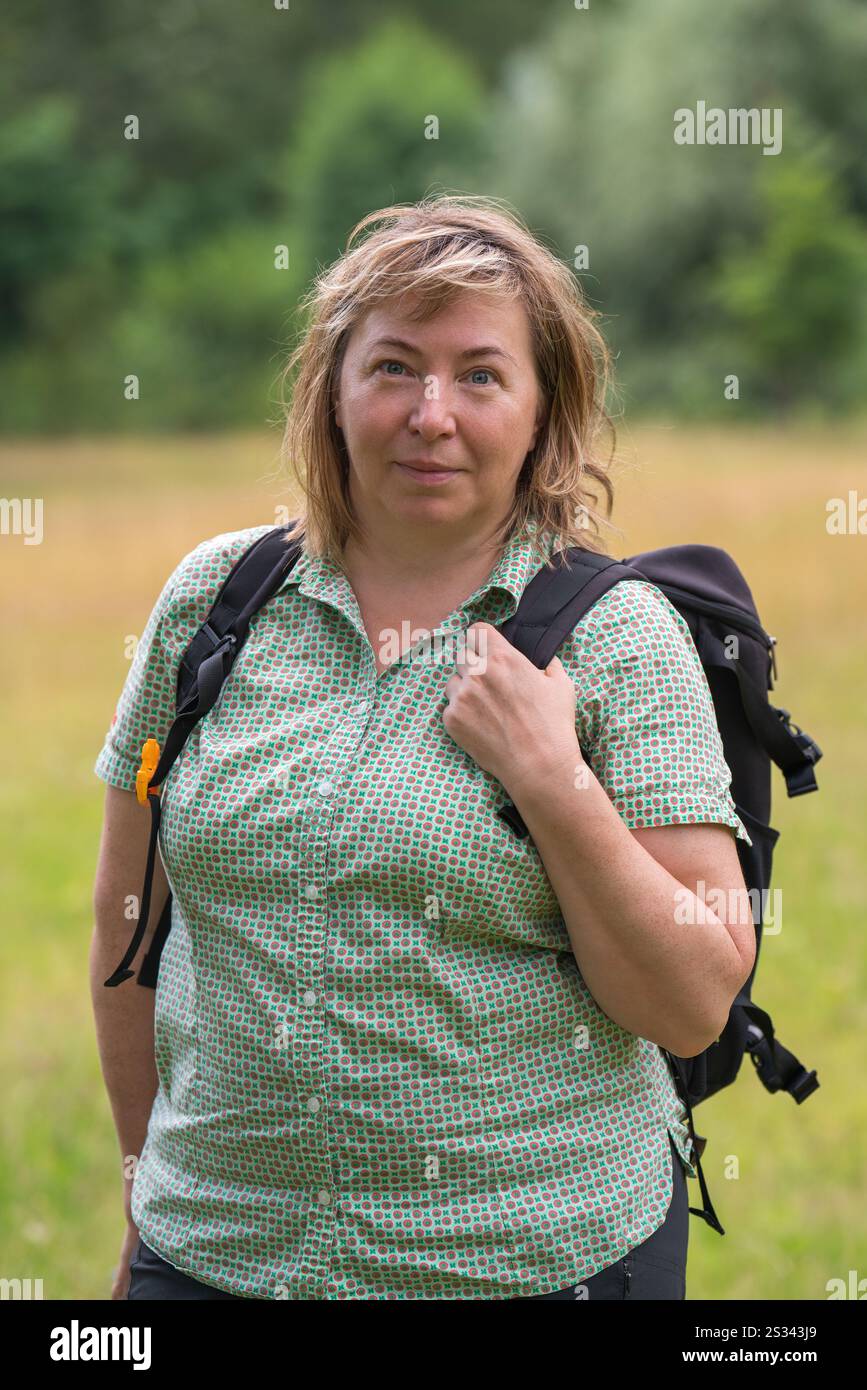 Eine gewöhnliche Frau mittleren Alters mit Rucksack lächelt beim Wandern und besucht neue Orte. Aktiver Lebensstil. Stockfoto