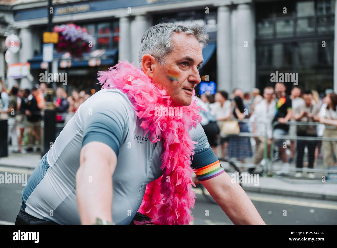 Radfahrer bei der Pride of London Parade, die mit rosa Boa und Regenbogenkleidung geschmückt ist. 2024 Stockfoto