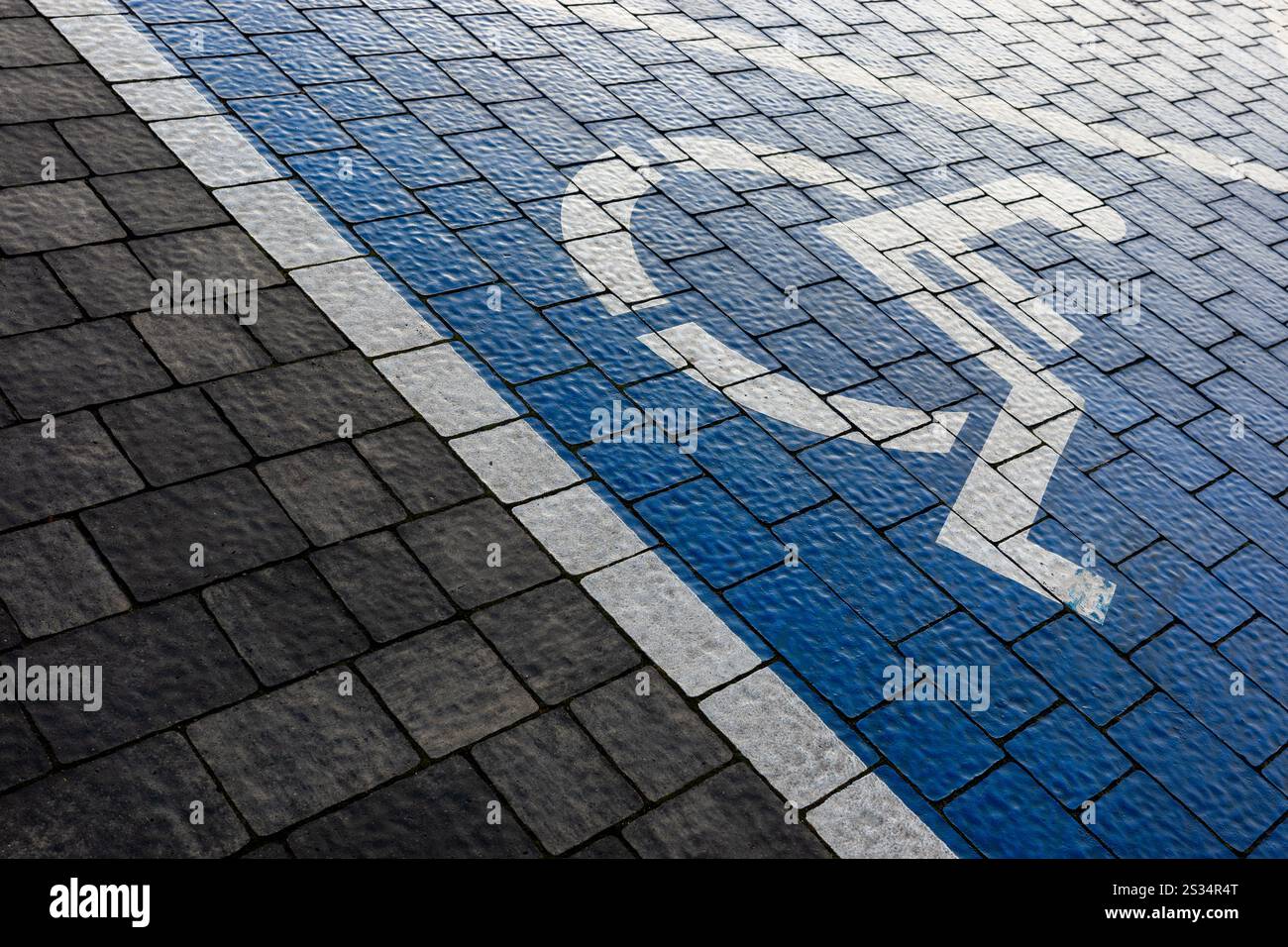 Weiß-blaue Markierung eines Behindertenparkplatzes auf einem Parkplatz aus grauen Blöcken. Eine Zeichnung eines Rollstuhls auf die Oberfläche gemalt. Stockfoto