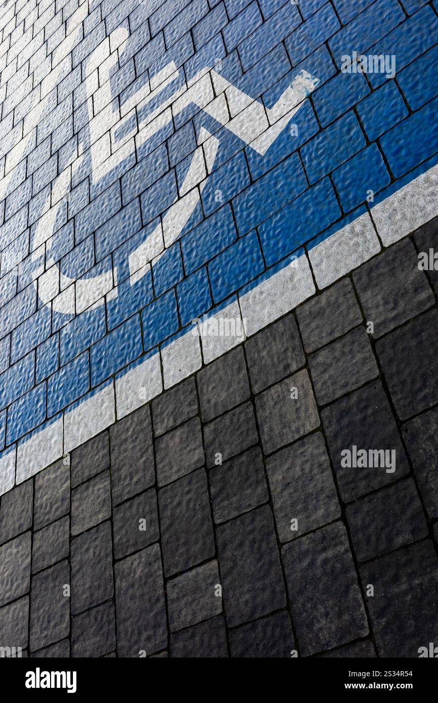Weiß-blaue Markierung eines Behindertenparkplatzes auf einem Parkplatz aus grauen Blöcken. Eine Zeichnung eines Rollstuhls auf die Oberfläche gemalt. Stockfoto