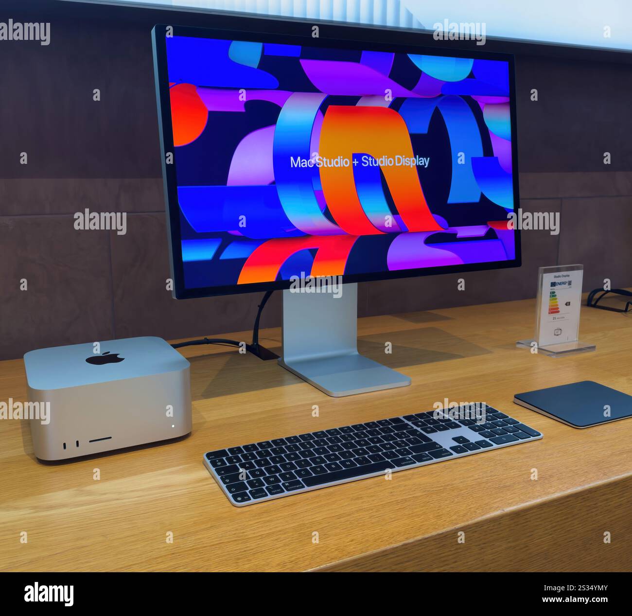 Paris, Frankreich - 10. Dezember 2024: Ein elegantes Mac Studio-Setup mit lebendigem Studio-Display, Tastatur und Trackpad auf einem Holztisch. Eine Produktinformationskarte ist ebenfalls sichtbar. Stockfoto