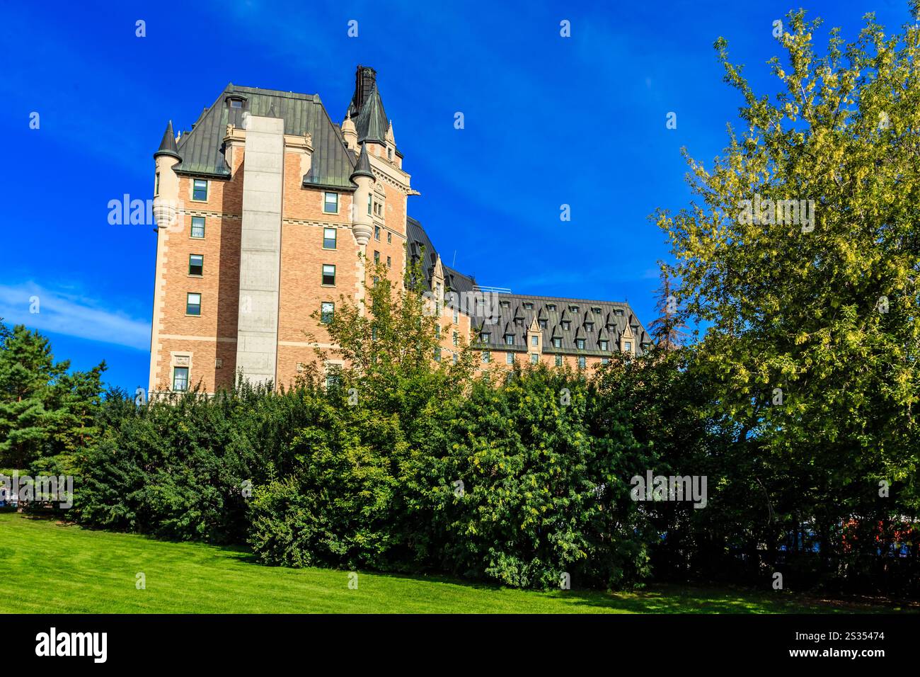 Ein großes Gebäude mit einem grünen Dach und einem grünen Baum davor. Das Gebäude ist hoch und hat viele Fenster. Der Himmel ist blau und klar Stockfoto