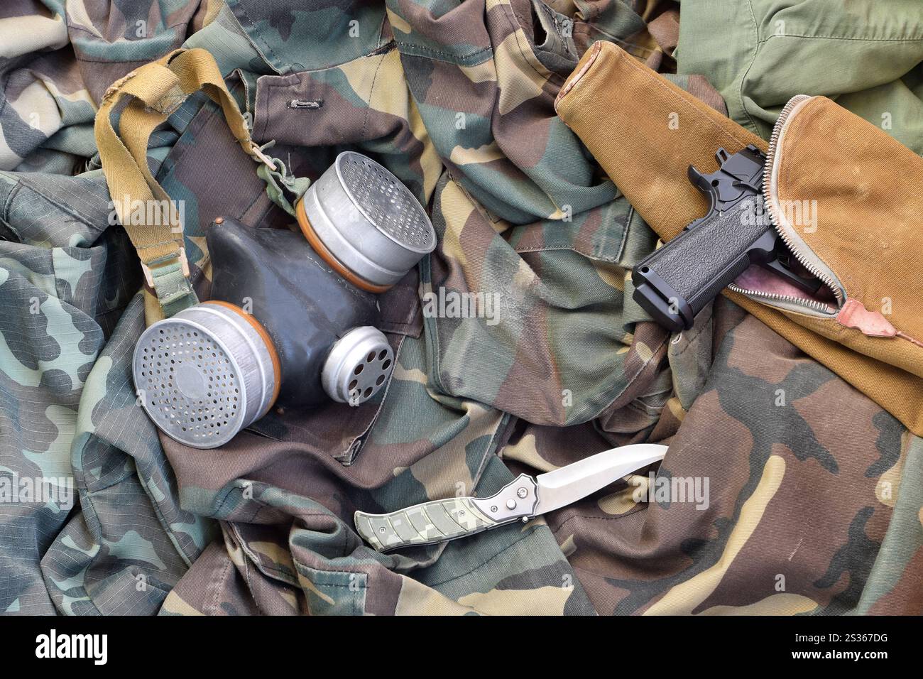 Stalker Soldaten sowjetischen Gasmaske liegen mit Handfeuerwaffe und Messer auf grünen Khaki-Tarnjacken. Set mit überlebenden Artikeln nach der Apokalypse Stockfoto