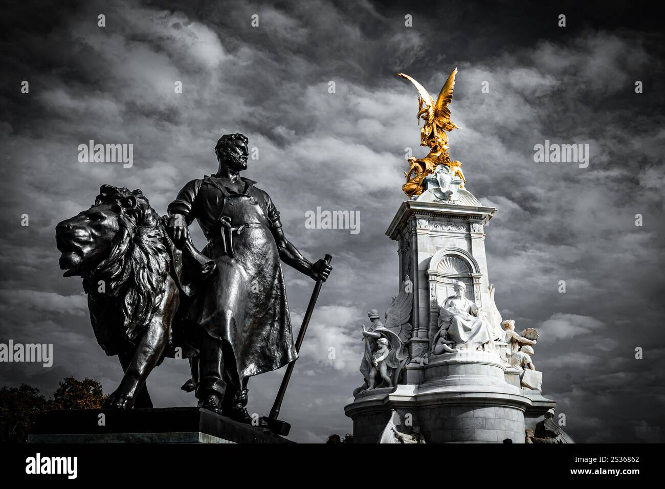 Die Statue eines Mannes neben einem Löwen ist Teil des Queen Victoria Memorial auf dem Platz vor dem Buckingham Palace in London. Stockfoto