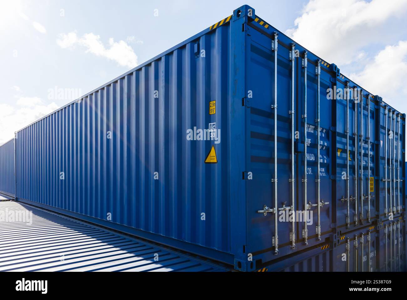 Blaue Frachtcontainer werden tagsüber im Lagerbereich unter bewölktem Himmel gestapelt Stockfoto