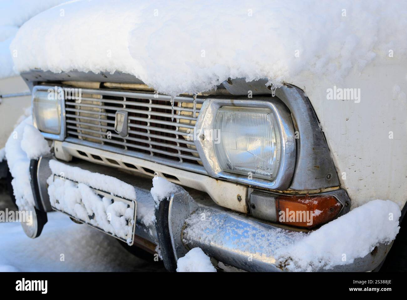 Altes Retro-Auto unter schneebedeckten Scheinwerfern mit verchromtem Kühlergrill und detailliertem Foto am Stoßfänger. Altes Retro-Auto unter dem schneebedeckten Fotoscheinwerfer mit Chrom Stockfoto