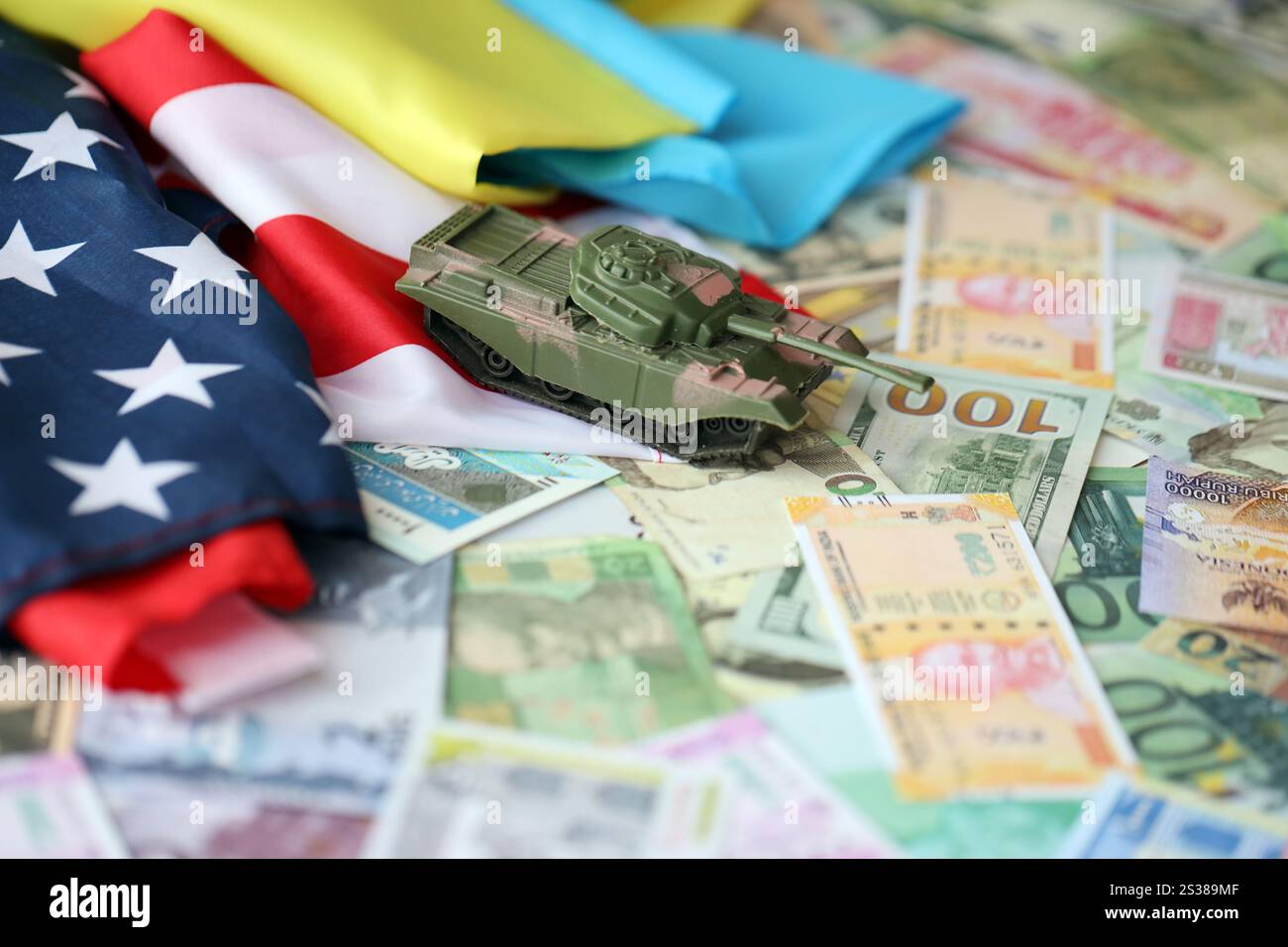 Spielzeugtank auf US-Flagge und ukrainische Flagge auf vielen Banknoten verschiedener Währungen. Hintergrund der Kriegsfinanzierung und der militärischen Unterstützung zwischen den Vereinigten Staaten Stockfoto