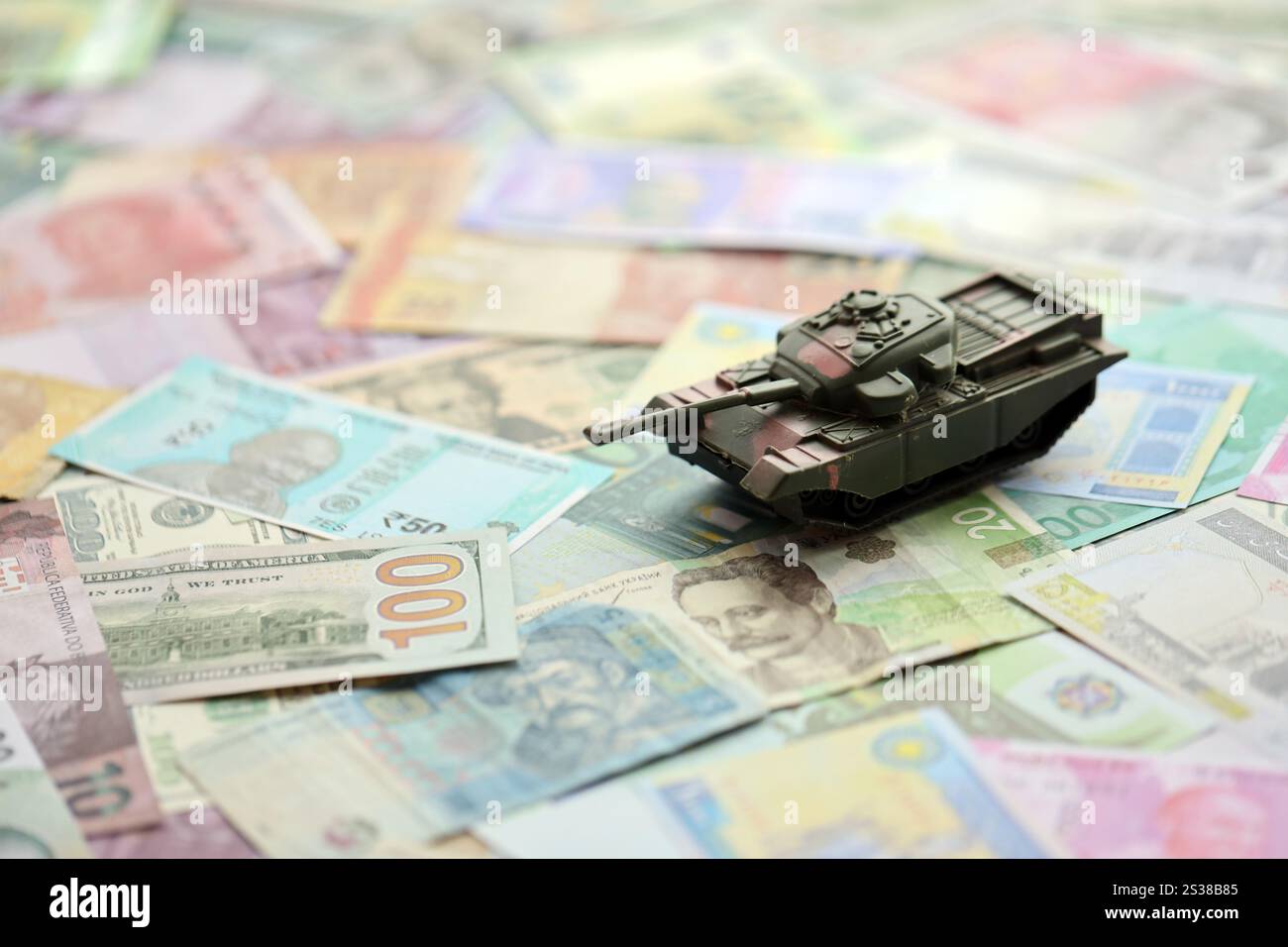Kleiner grüner Tank auf vielen Banknoten verschiedener Währungen. Hintergrund der Kriegsfinanzierung oder Geld für die Verteidigung aus der Nähe. Kleiner grüner Tank auf vielen Stockfoto