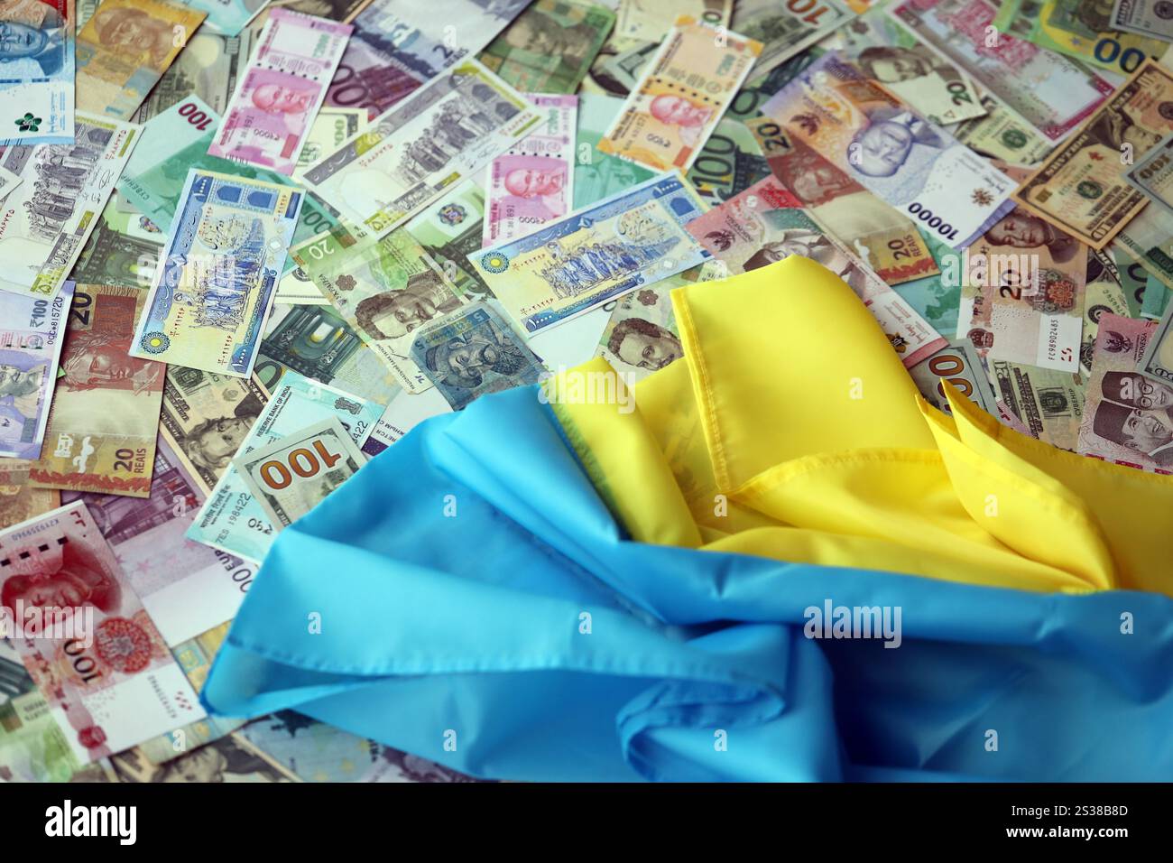 Ukrainische Flagge auf vielen Banknoten verschiedener Währungen. Hintergrund der Kriegsfinanzierung und des Preises für militärische Unterstützung in der Ukraine. Ukrainische Flagge auf vielen Stockfoto