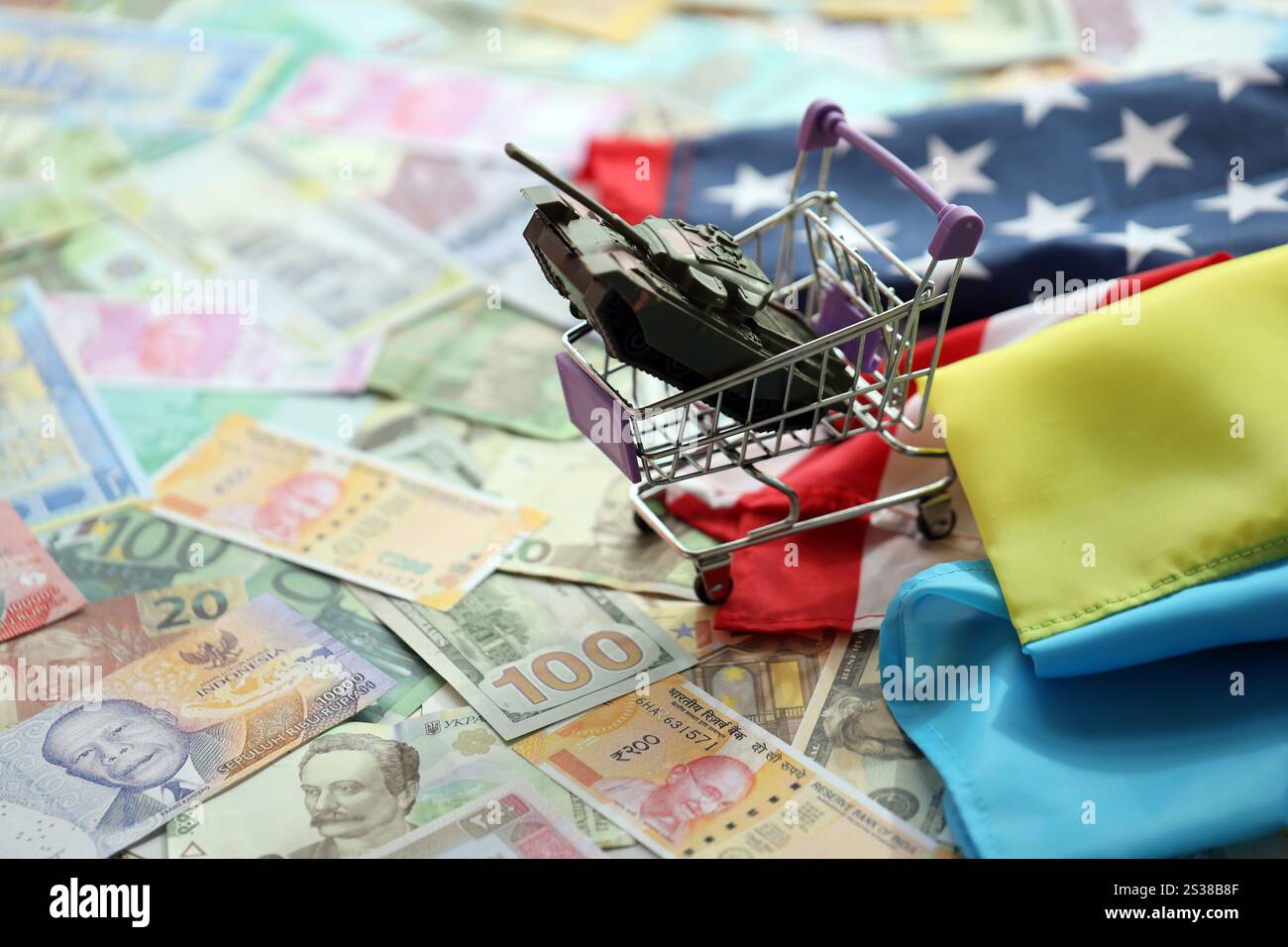 Spielzeugtank auf US-Flagge und ukrainische Flagge auf vielen Banknoten verschiedener Währungen. Hintergrund der Kriegsfinanzierung und der militärischen Unterstützung zwischen den Vereinigten Staaten Stockfoto