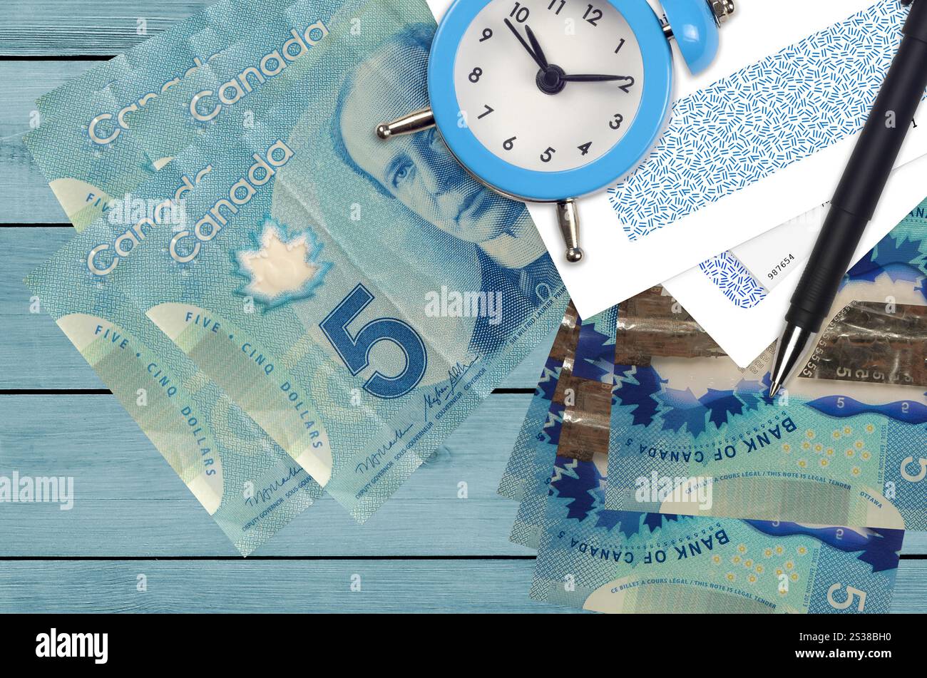 5 kanadische Dollar-Scheine und Wecker mit Stift und Umschlägen. Steuersaisonkonzept, Zahlungsfrist für Kredit oder Darlehen. Finanzoperationen verwenden Stockfoto