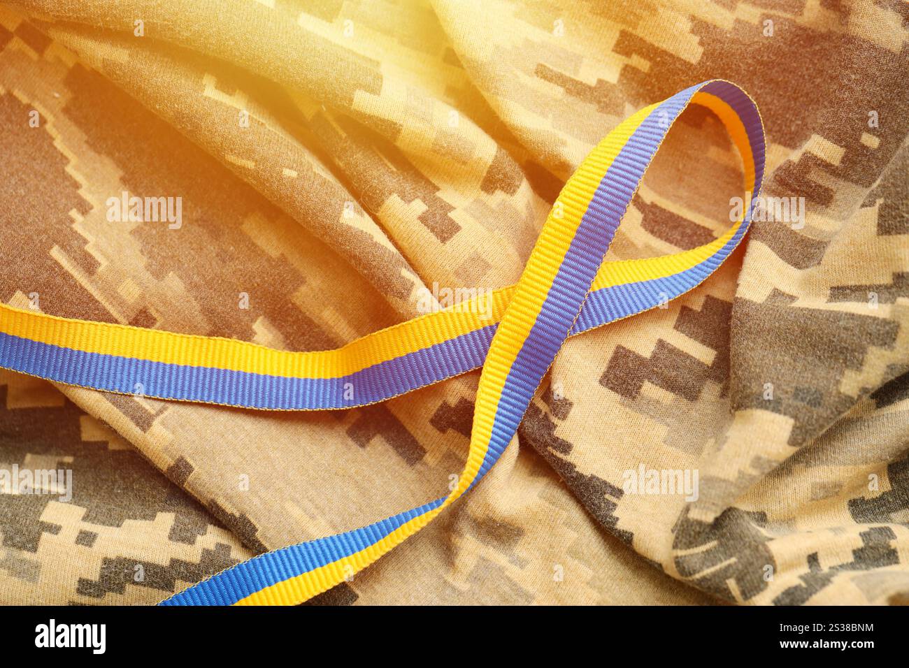Gepixelter, digitaler Militärtarnstoff mit Band in blauen und gelben Farben. Attribute der ukrainischen patriotischen Soldatenuniform. Gepixelt digital Stockfoto