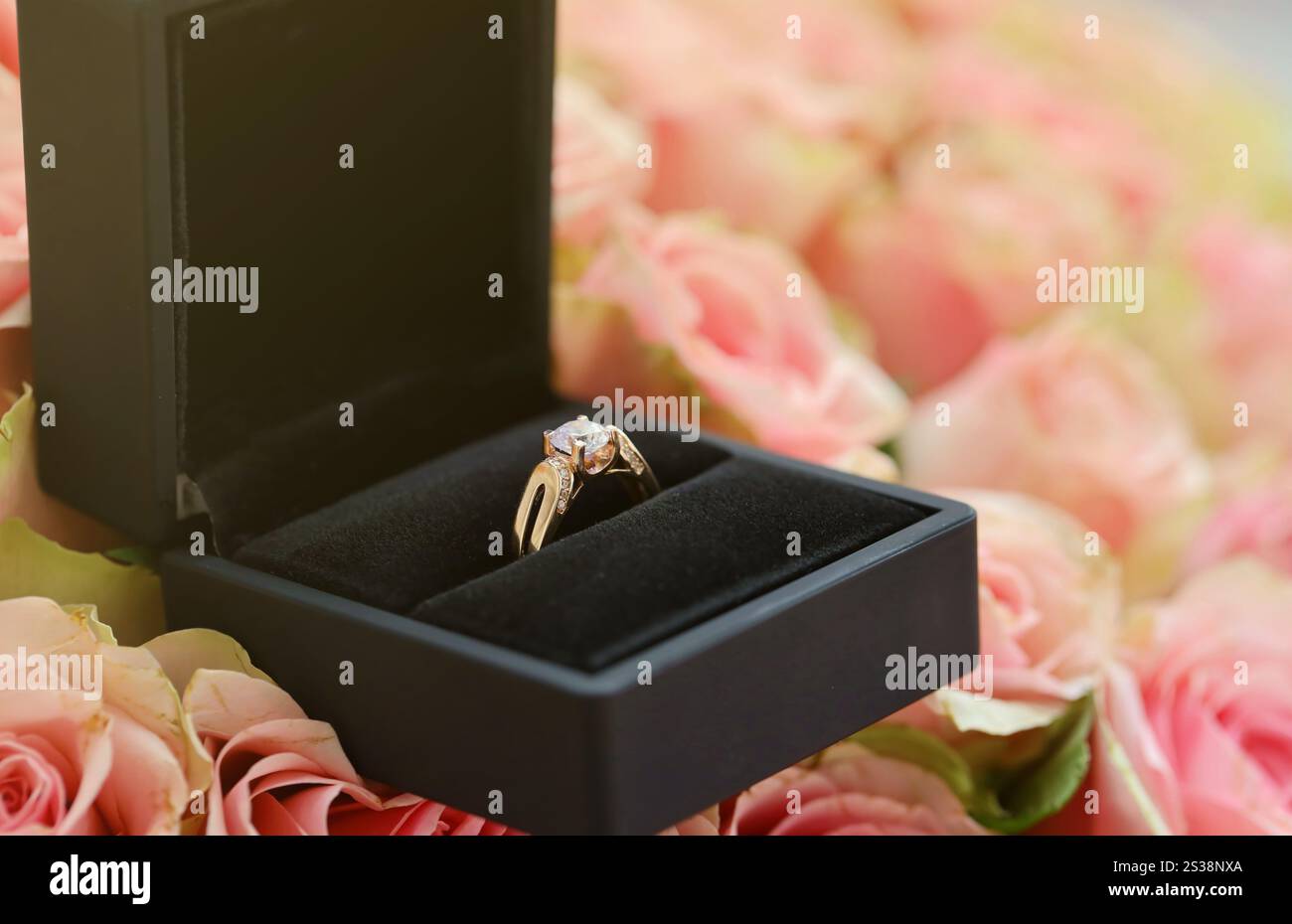Goldener Diamant-Verlobungsring im Black Box-Gehäuse zwischen einer großen Menge Rosen im großen Blumenstrauß Nahaufnahme mit verschwommenem Hintergrund. Gold Diamant-Einsatz Stockfoto