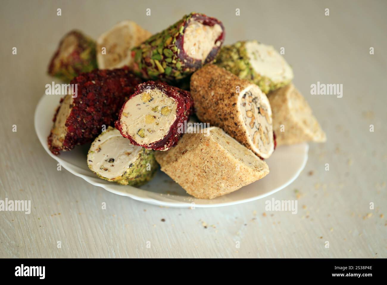 Viele Rollen türkischer Delikatesse mit verschiedenen Aromen und Füllungen auf weißem Teller auf dem Tisch. Teile von türkischen Lokumu-Süßigkeiten. Viele Rollen türkischer Delikatessen Stockfoto
