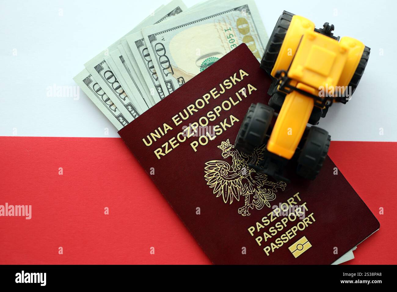 Roter polnischer Pass und gelber Traktor auf US-Geld und glatte rot-weiße Flagge von Polen Nahaufnahme. Roter polnischer Pass und gelber Traktor in den USA Stockfoto