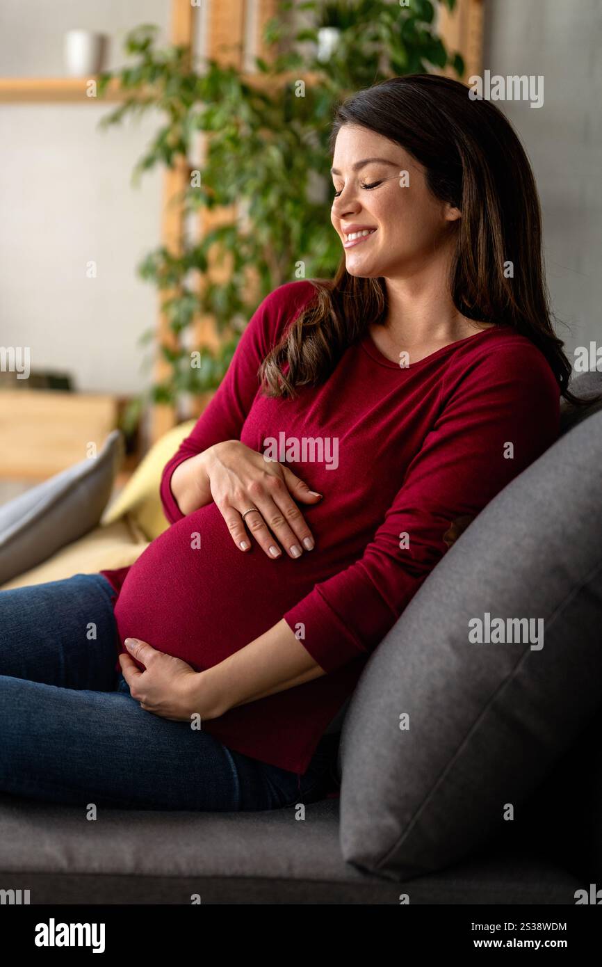 Schwangere Frau wird auf dem Bett ausgeruht gesehen. Sie wirkt zufrieden und gelassen und genießt einen ruhigen Moment Stockfoto