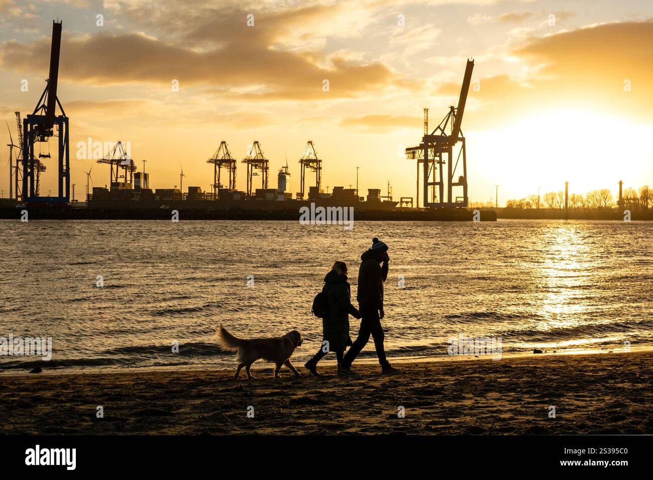 Menschen gehen mit ihrem Hund an der Hamburger Elbe vor dem Hafenviertel bei Sonnenuntergang Stockfoto