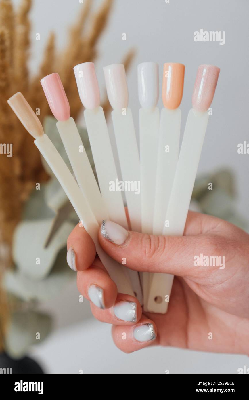 Eine Hand, die eine nagellack-Musterpalette in sanften neutralen Tönen hält. Perfekt für Beauty-, Maniküre- und Nageldesign. Elegante und moderne Präsentation Stockfoto