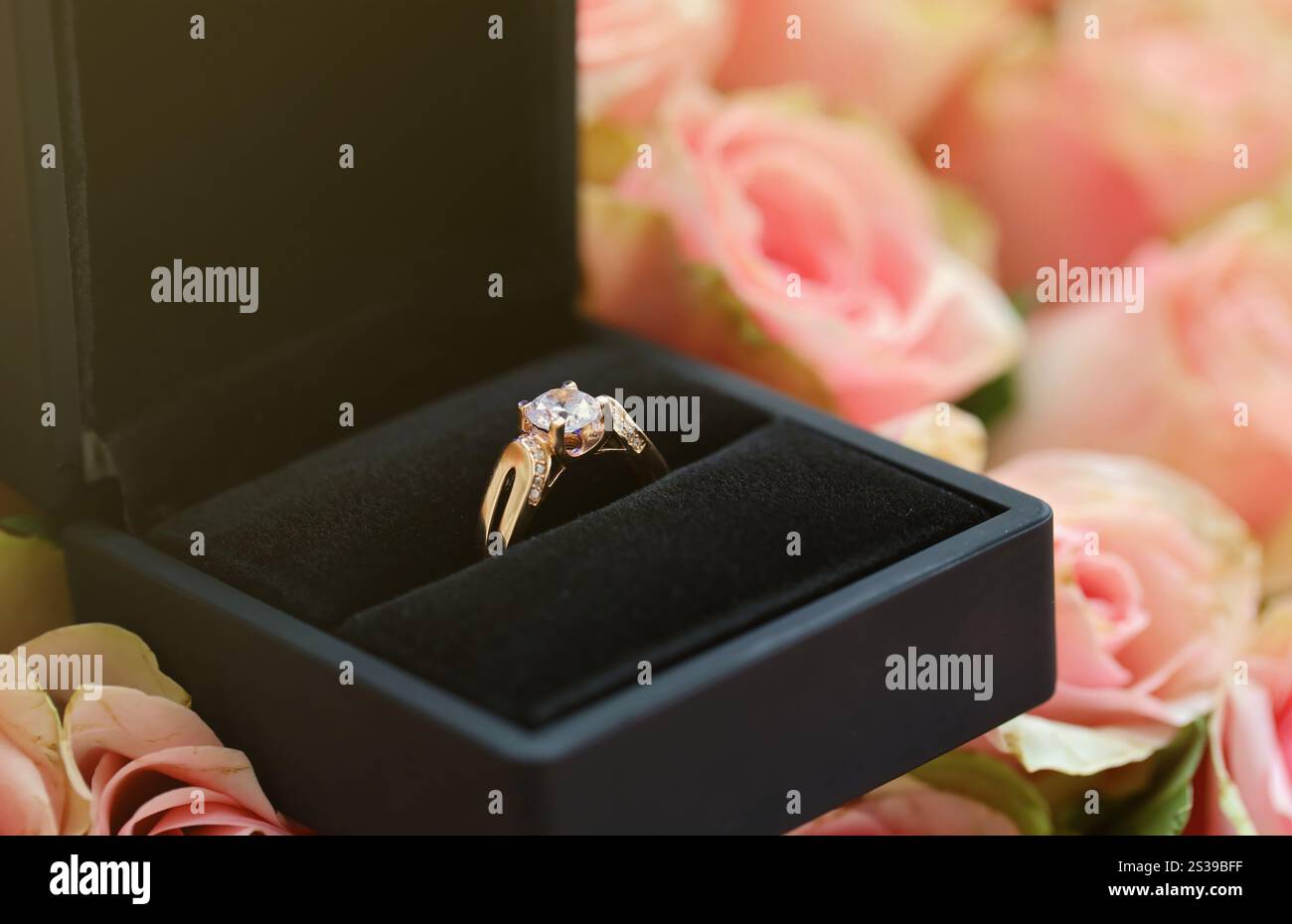 Goldener Diamant-Verlobungsring im Black Box-Gehäuse zwischen einer großen Menge Rosen im großen Blumenstrauß Nahaufnahme mit verschwommenem Hintergrund. Gold Diamant-Einsatz Stockfoto