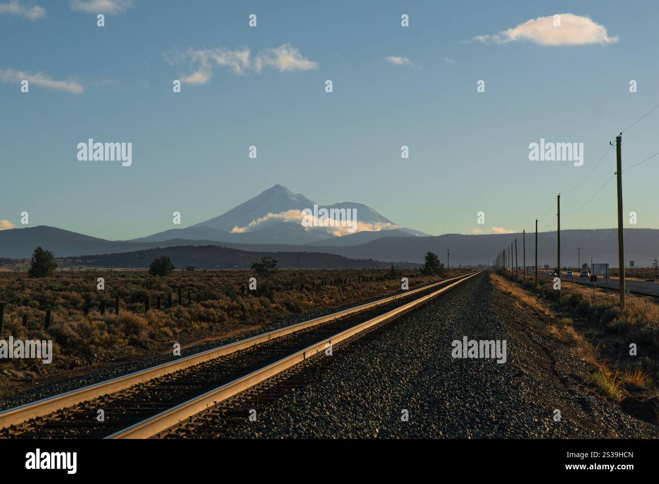 Gerade Bahngleise, die auf den schneebedeckten Gipfel des Mount Shasta zuführen, der bei Sonnenuntergang im Winterlandschaf Nordkaliforniens leuchtet, USA Stockfoto