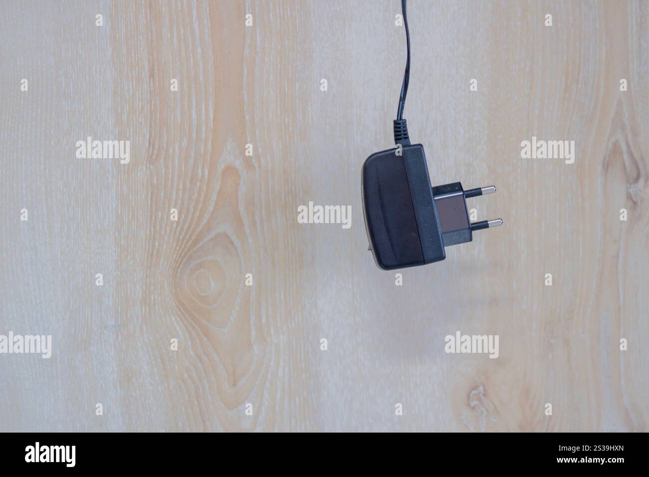 Ein schwarzes Netzkabel hängt über einem hölzernen Wandhintergrund. Elektrizitäts- und Energieeffizienzkonzept. Vorderansicht, Kopierraum. Stockfoto