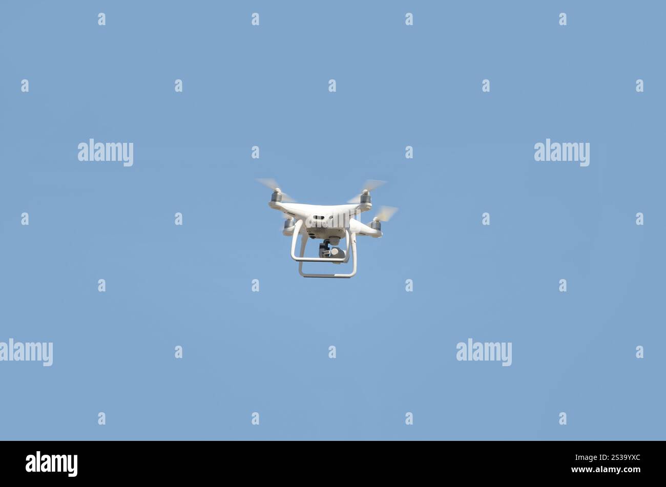 Große weiße Drohne, die in einem hellen wolkenlosen blauen Himmel schwebt, Funksteuerhubschrauber mit tragbarer Videokamera-Versorgung. Große weiße Drohne, die in A schwebt Stockfoto