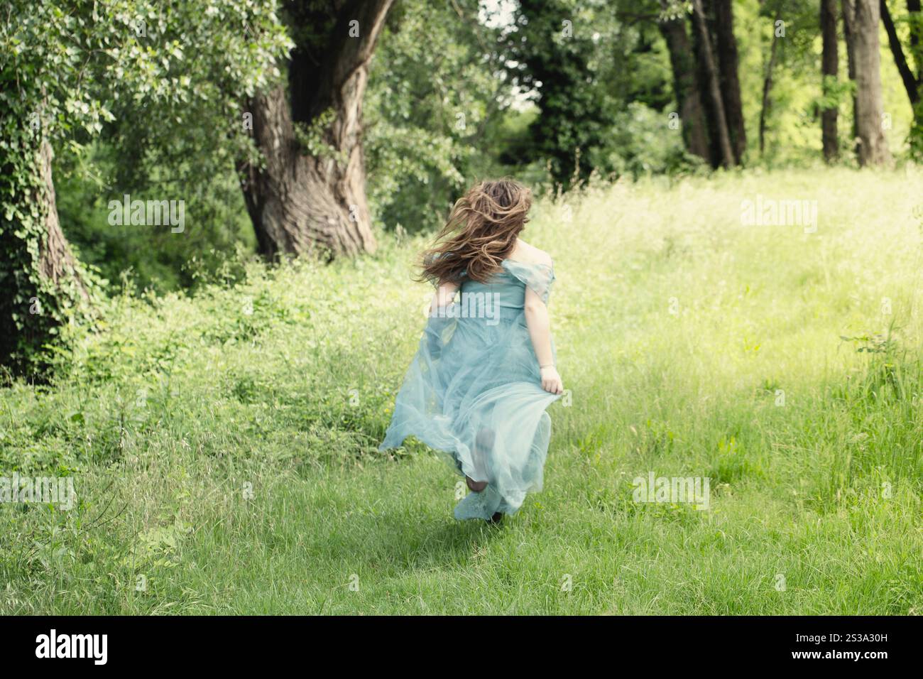 Elegante Frau, die auf einer Wiese mit flatterndem Kleid läuft, Freiheitskonzept Stockfoto