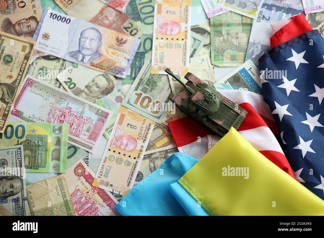 Spielzeugtank auf US-Flagge und ukrainische Flagge auf vielen Banknoten verschiedener Währungen. Hintergrund der Kriegsfinanzierung und der militärischen Unterstützung zwischen den Vereinigten Staaten Stockfoto