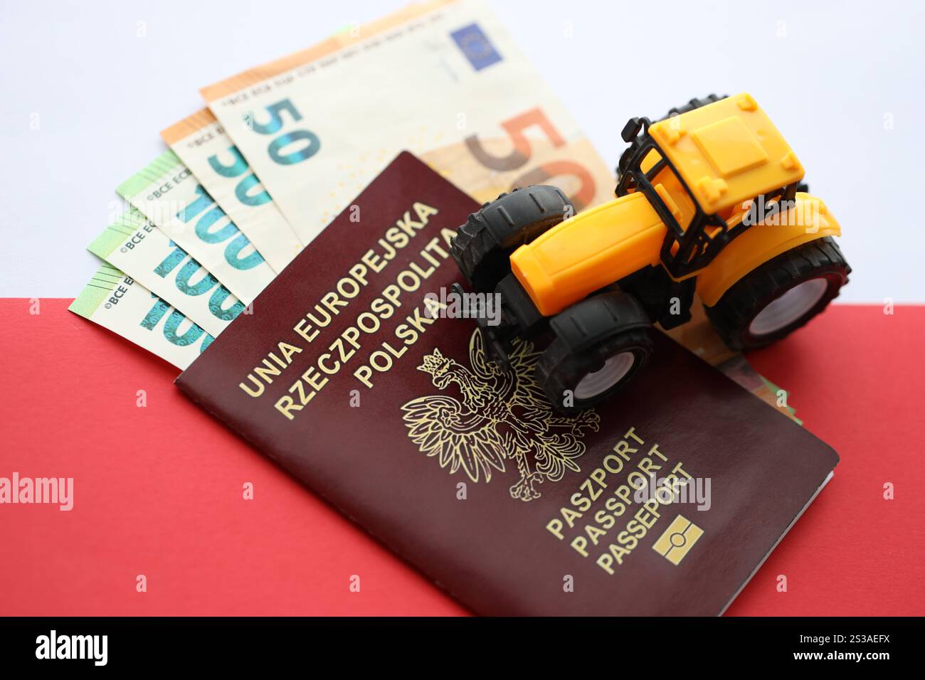 Roter polnischer Pass und gelber Traktor auf Euro-Geld und glatte rot-weiße Flagge von Polen aus nächster Nähe. Roter polnischer Pass und gelber Traktor auf Euro Stockfoto