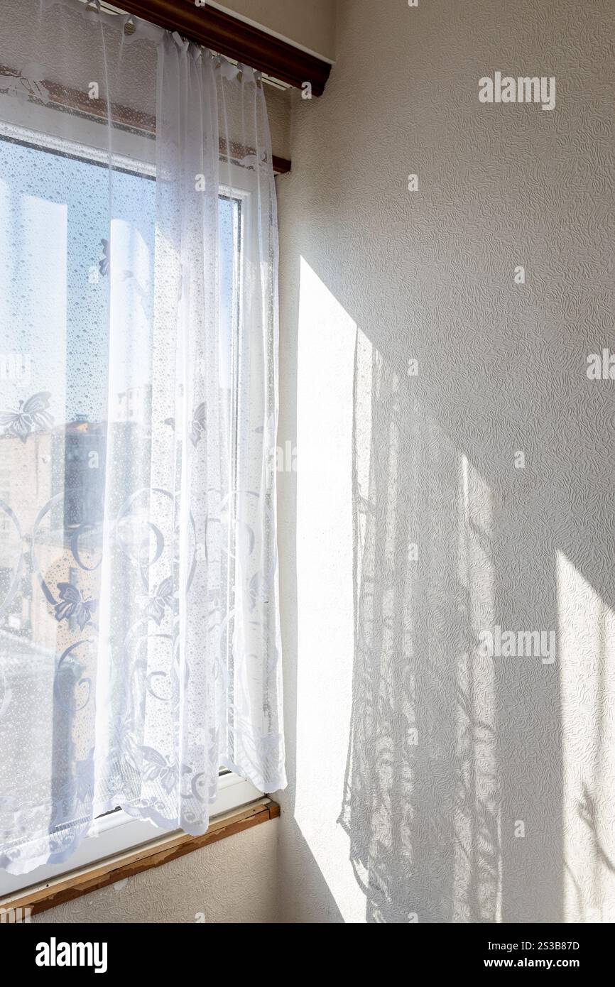 tüll-Vorhänge am Fenster und an der Wand, beleuchtet von der Sonne und Blick auf die städtischen Häuser im Hintergrund Stockfoto