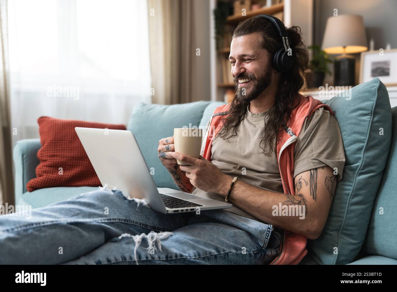 Junger Mann, der ein Notebook nutzt und zu Hause Musik hört, während er als Experte für globale Geschäftsmärkte arbeitet. Freiberufliche Arbeit Berufsberuf Web de Stockfoto