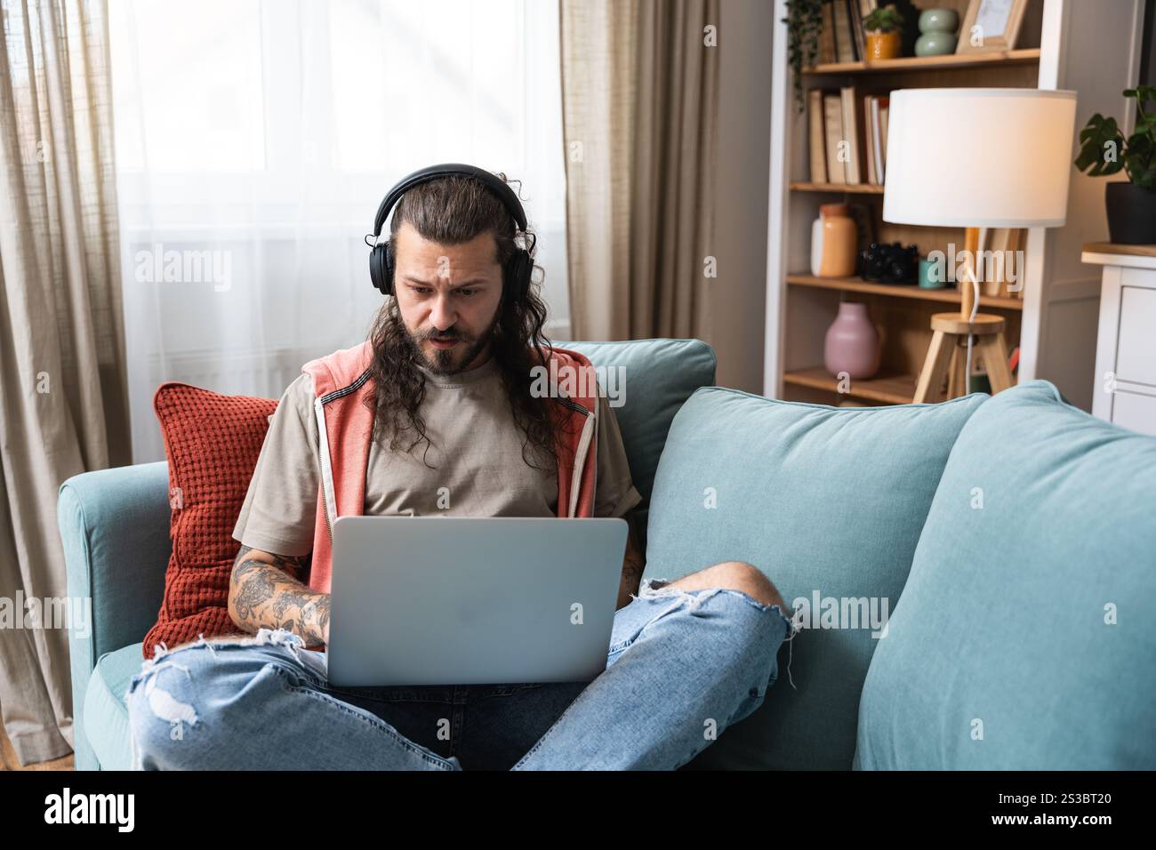 Junger Mann, der ein Notebook nutzt und zu Hause Musik hört, während er als Experte für globale Geschäftsmärkte arbeitet. Freiberufliche Arbeit Berufsberuf Web de Stockfoto