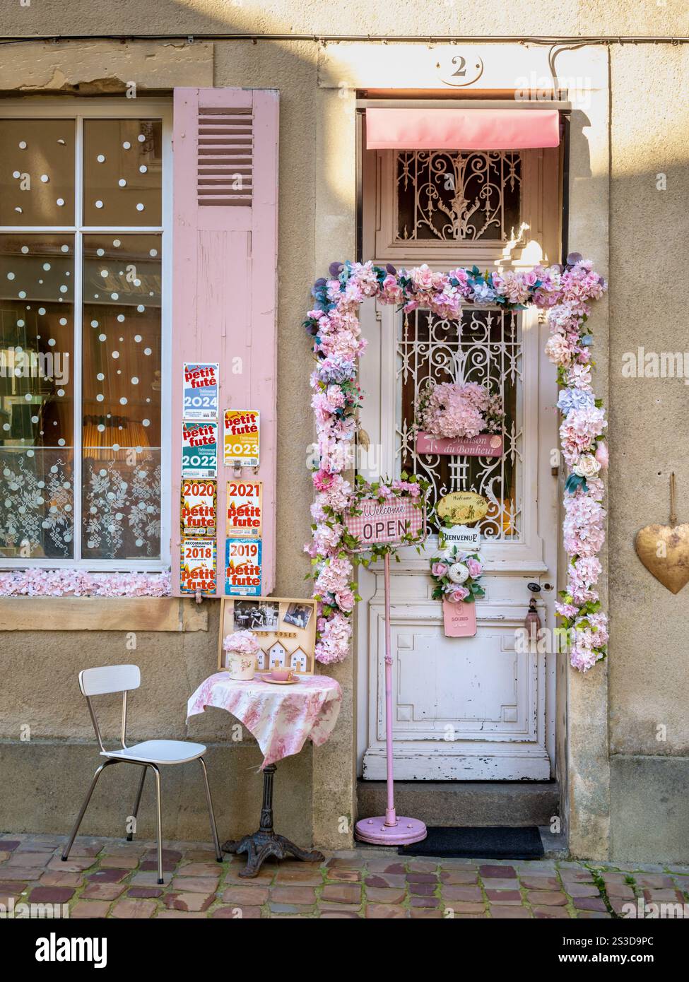Die charmante rosafarbene Fassade und der mit Blumen dekorierte Eingang des Teehauses Les Volets Roses salon de thé in Bayeux, Normandie, Frankreich Stockfoto