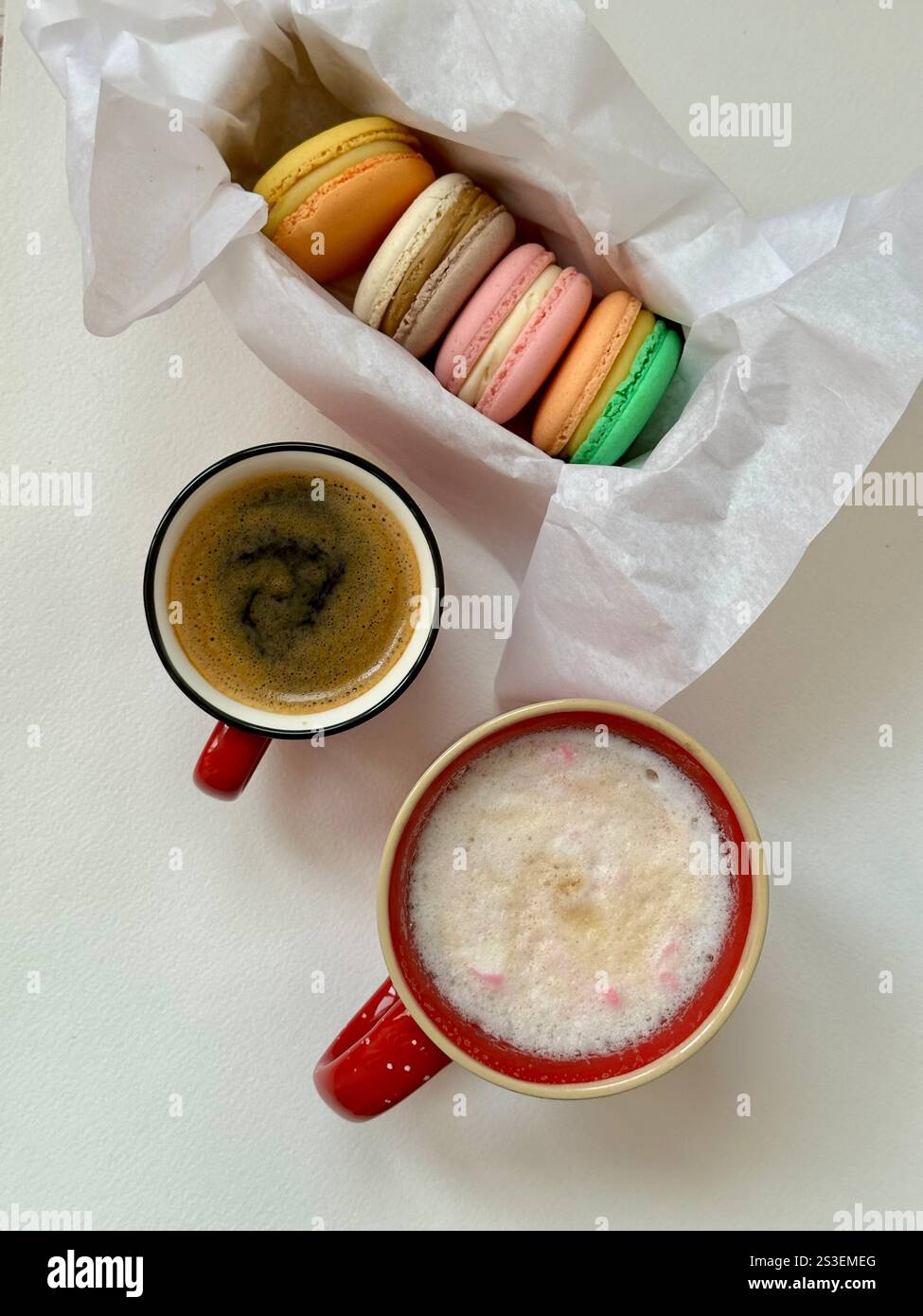 Macarons in verschiedenen Farben und Geschmacksrichtungen in der Schachtel und Tassen Kaffee - Smartphone-aufgenommenes Stockfoto